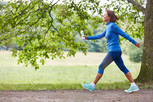 Frau mit fröhlichem Gesicht walkt in sportlicher Bekleidung im Park an einem grün belaubten Baum vorbei.